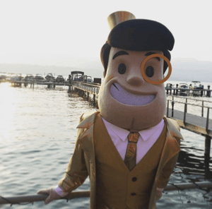 The Capitalist mascot standing next to a lake